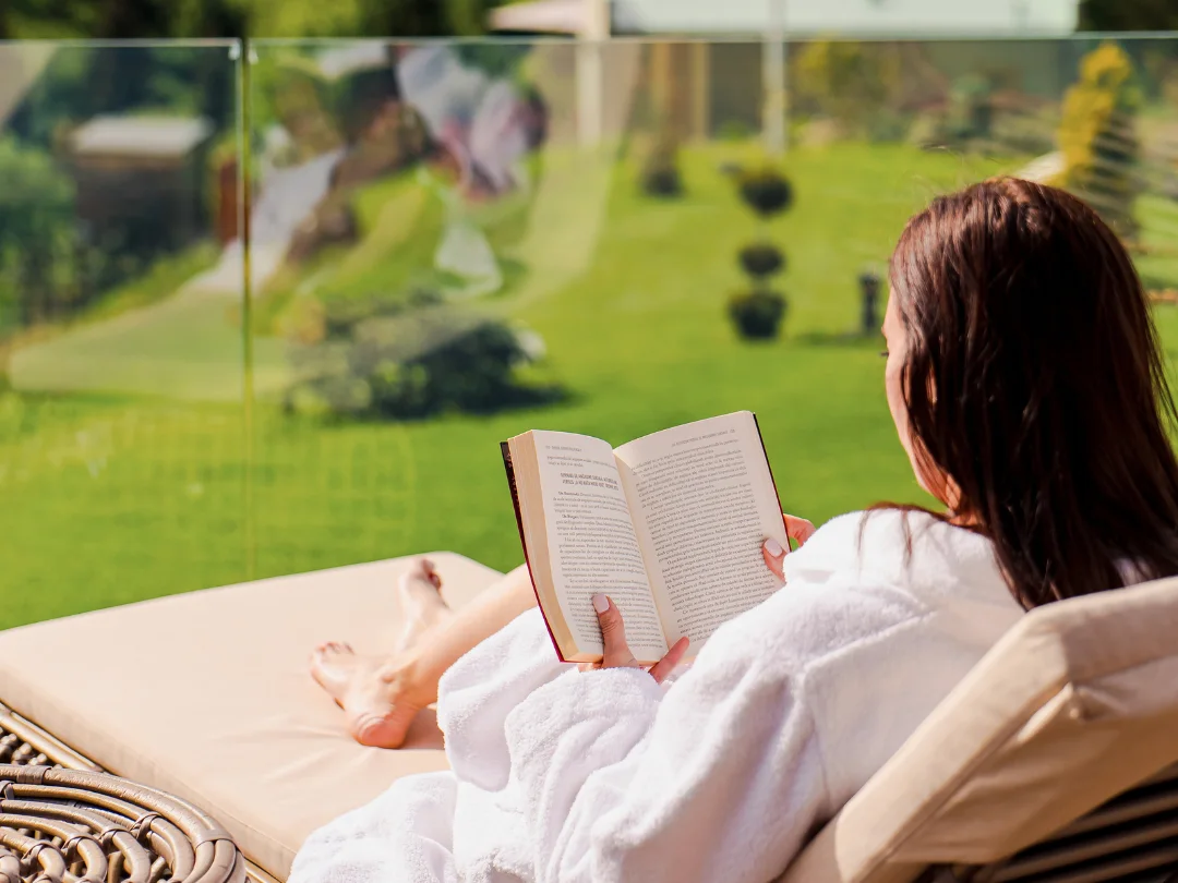 Woman in a white robe reading on an Eden Hill terrace lounger beside the lawn.