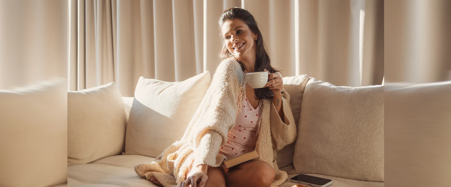 Woman holding a white mug on a cream sofa in a sunlit Eden Hill interior.