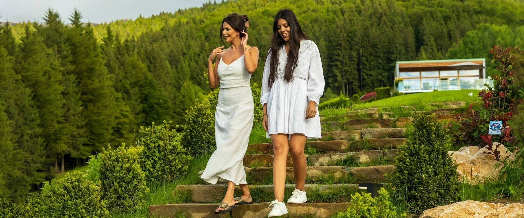 Two women walking down the steps in the Eden Hill garden between a villa and the forest.