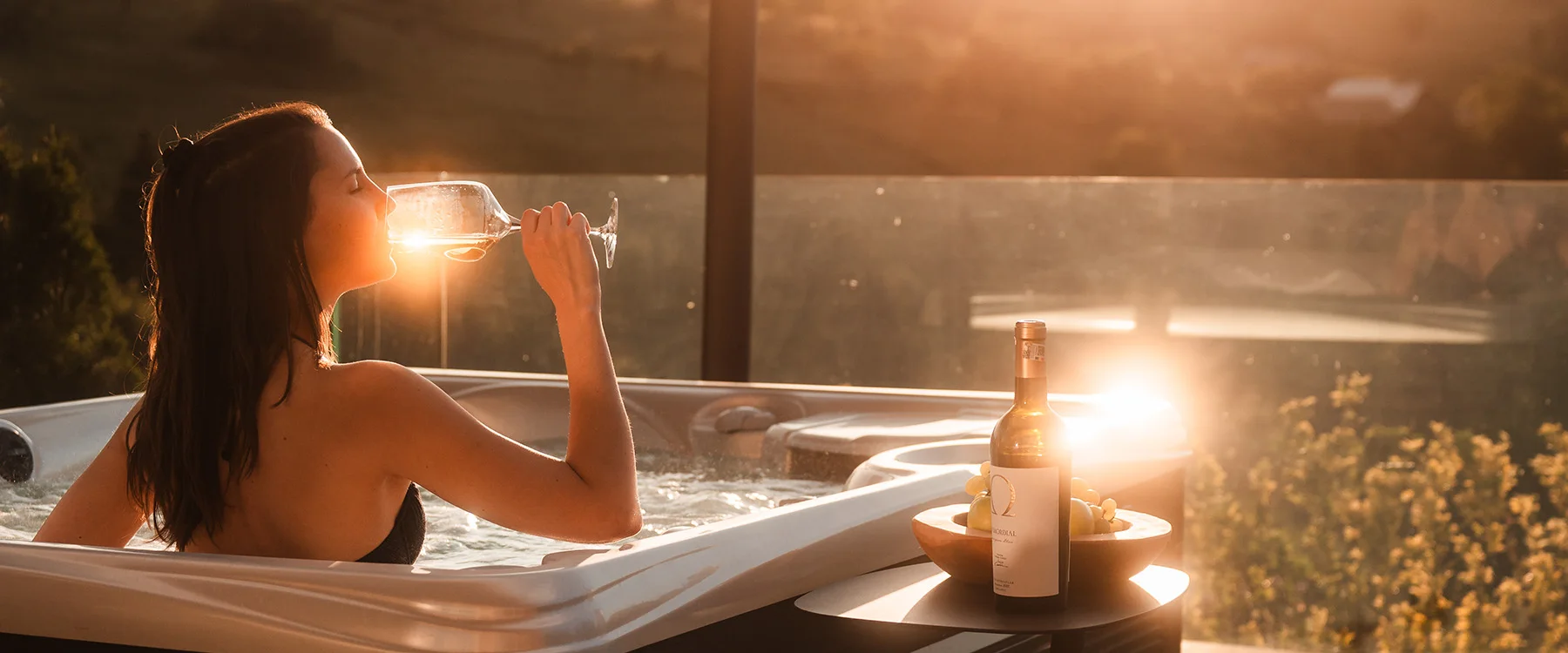 Woman holding a glass in an Eden Hill terrace hot tub at sunset.