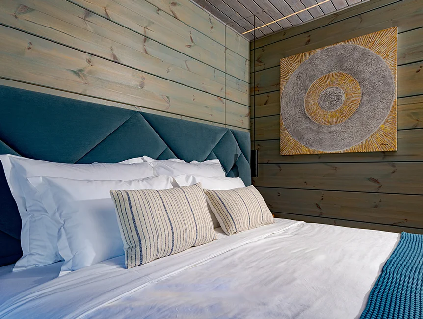 Bed with white pillows and a green headboard beside a decorated wooden wall in an Eden Hill bedroom.