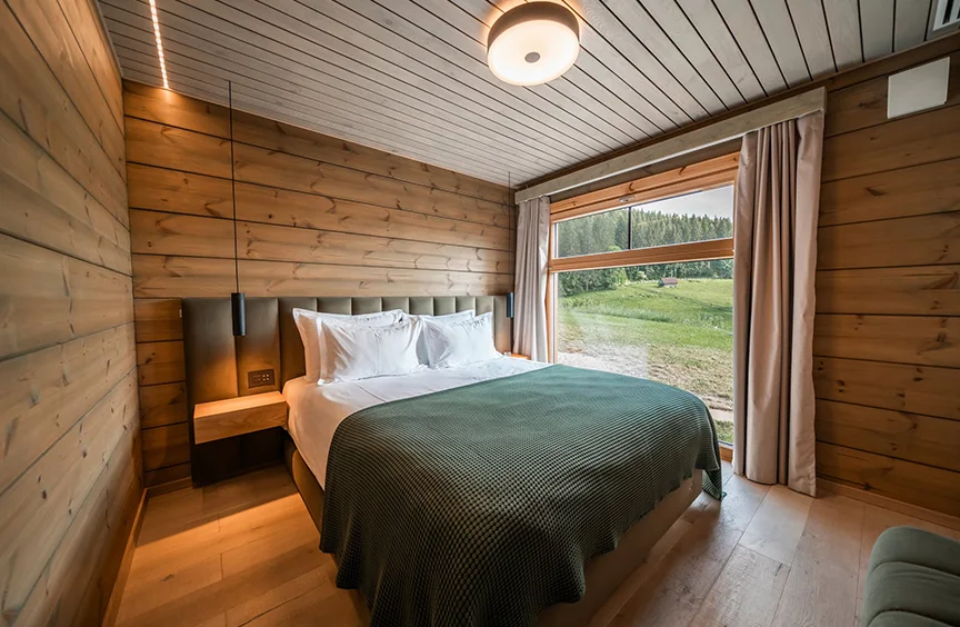 Eden Hill bedroom with wooden walls and a green bedspread, overlooking the lawn and forest.