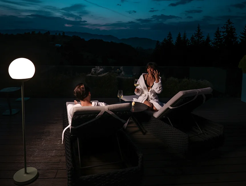 Couple on Eden Hill terrace loungers beside a glowing round lamp at night.