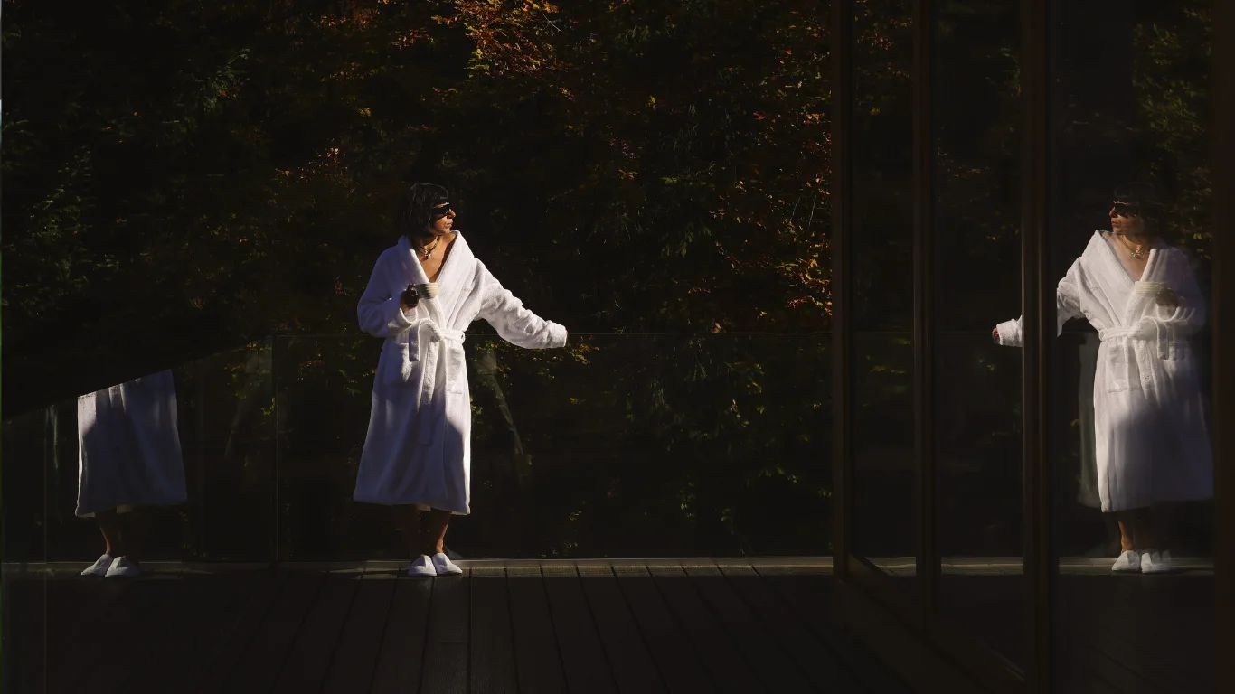 Woman in a white robe on an Eden Hill terrace, reflected in the villa's glass door.