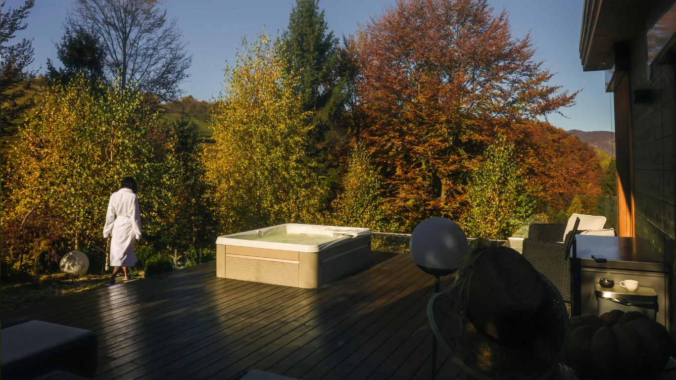 Woman in a white robe beside an Eden Hill terrace hot tub, surrounded by autumn trees.