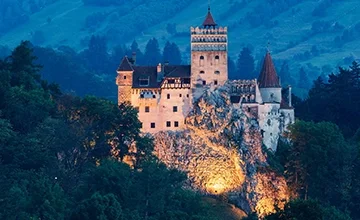 Bran Castle illuminated at dusk above the forest.