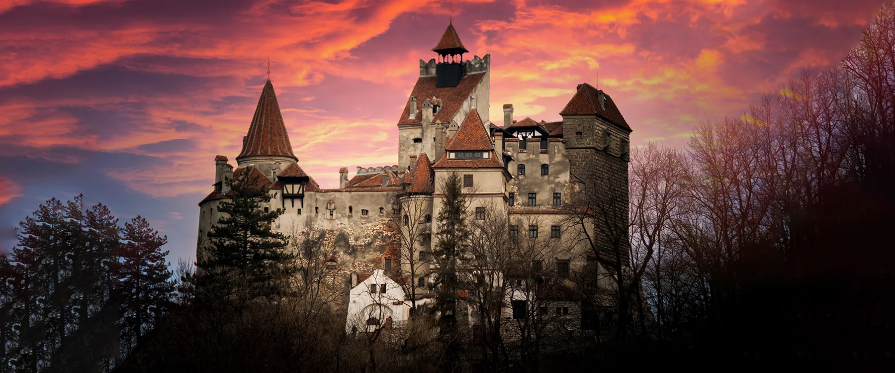 Castelul Bran sub un cer portocaliu-roșiatic la apus.