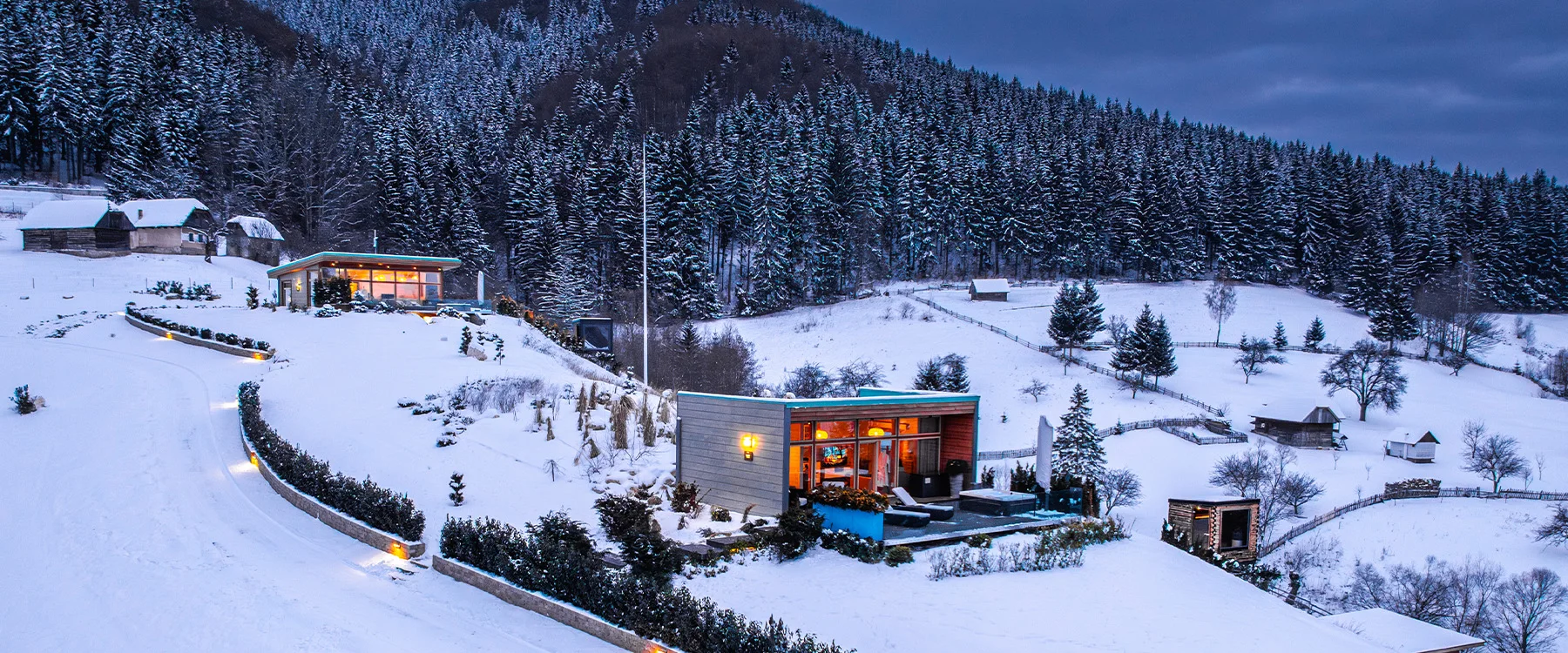 Aerial view of illuminated Eden Hill villas in a winter landscape beside a snow-covered forest.