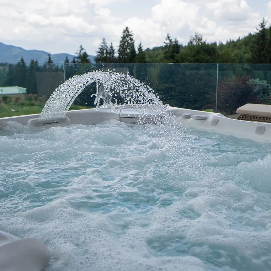 Water jet arcing over an Eden Hill hot tub, with forest and mountains in the background.