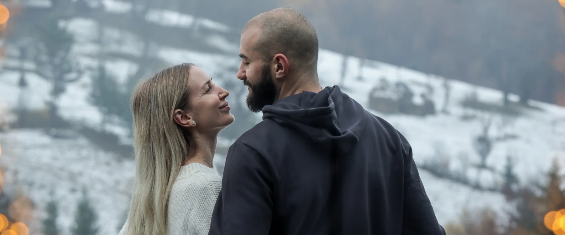 Couple facing each other outdoors, with a snowy valley in the background.