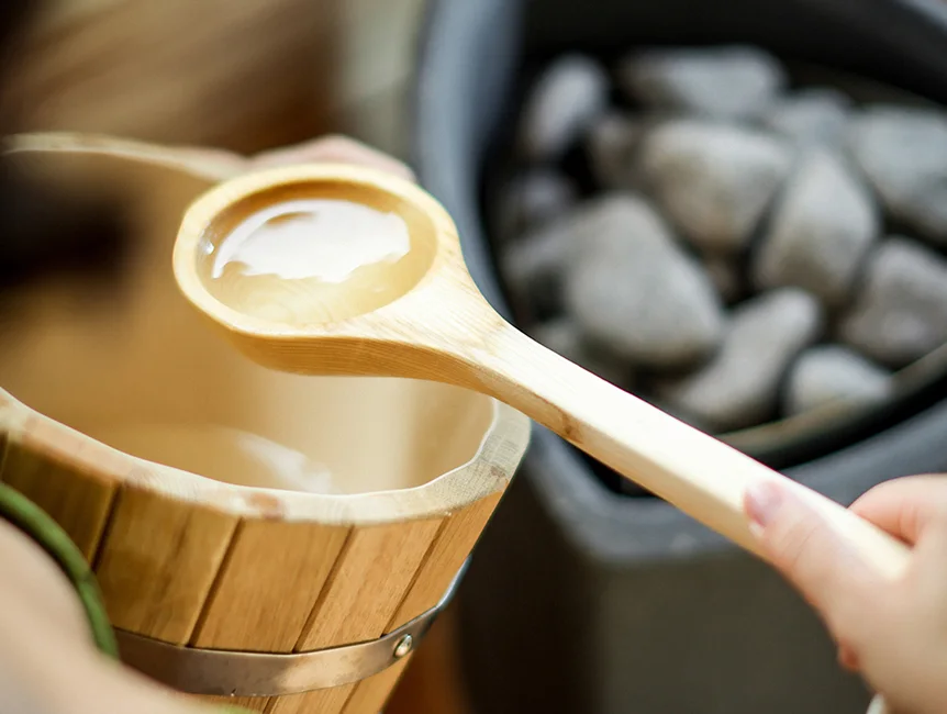 Water poured from a wooden ladle beside heated sauna stones.