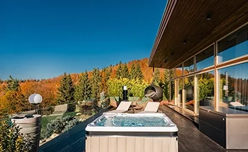 Eden Hill villa terrace with a hot tub and loungers, surrounded by orange autumn forest.