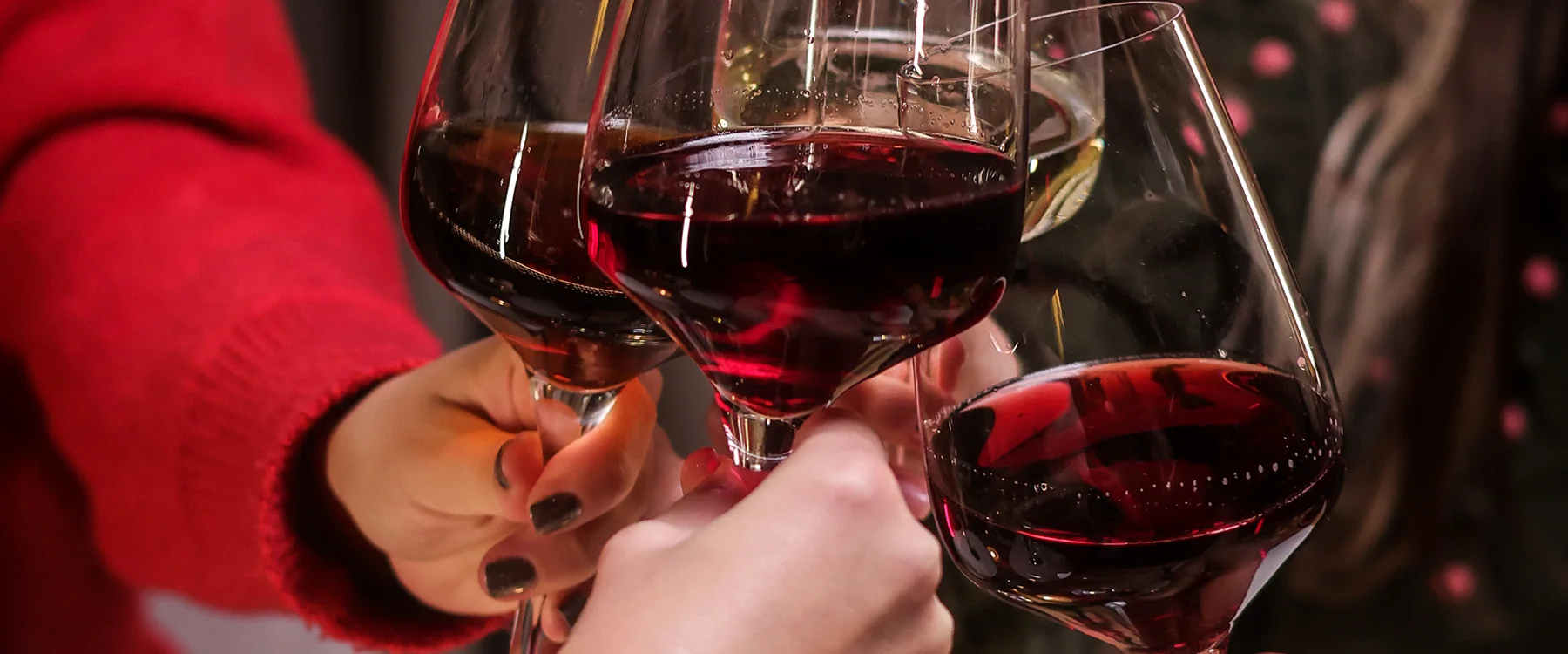 Glasses of red wine clinking above a table.