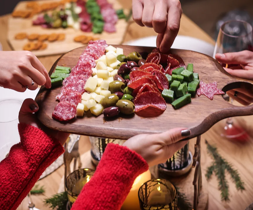 Several people sharing a platter of cheese, cured meats, grapes and vegetables at a table.