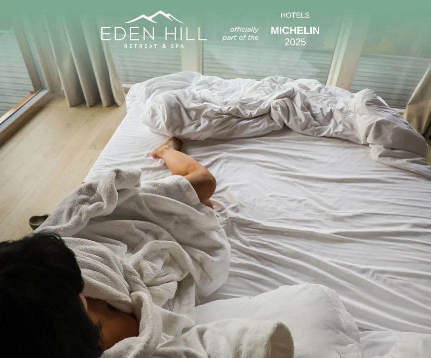 Woman relaxing in a bed with white linen in an Eden Hill composition featuring the Michelin Hotels 2025 badge.