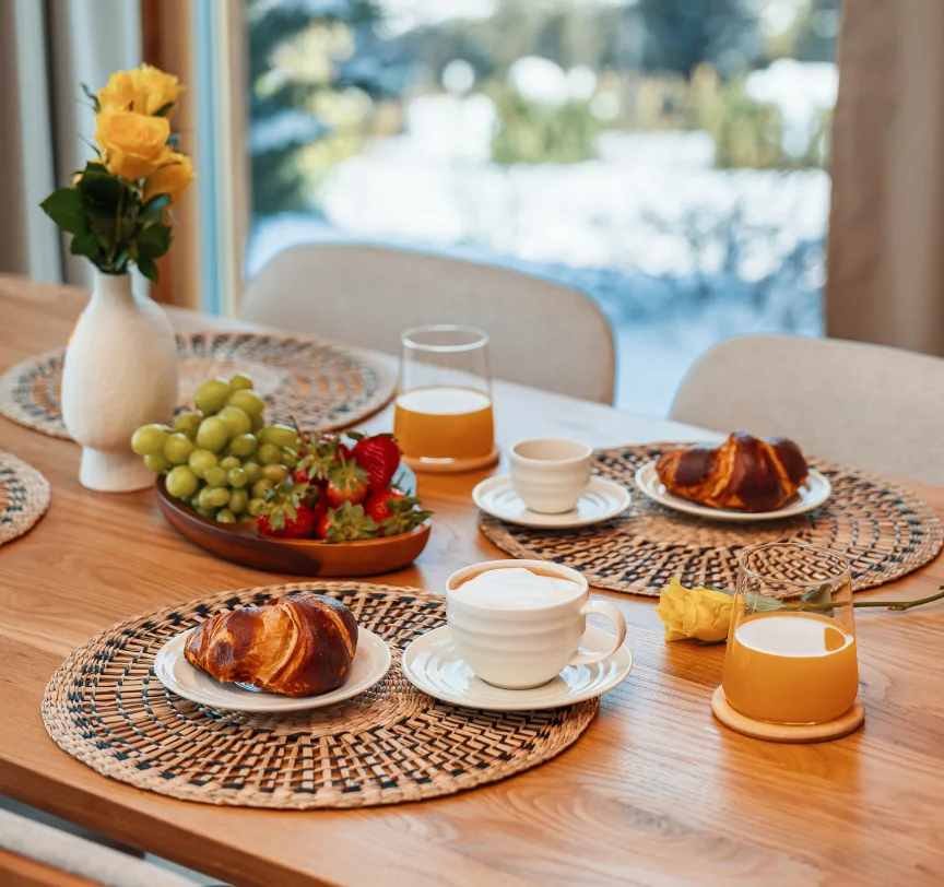 Breakfast for two with croissants, coffee, juice and fruit on a wooden table.