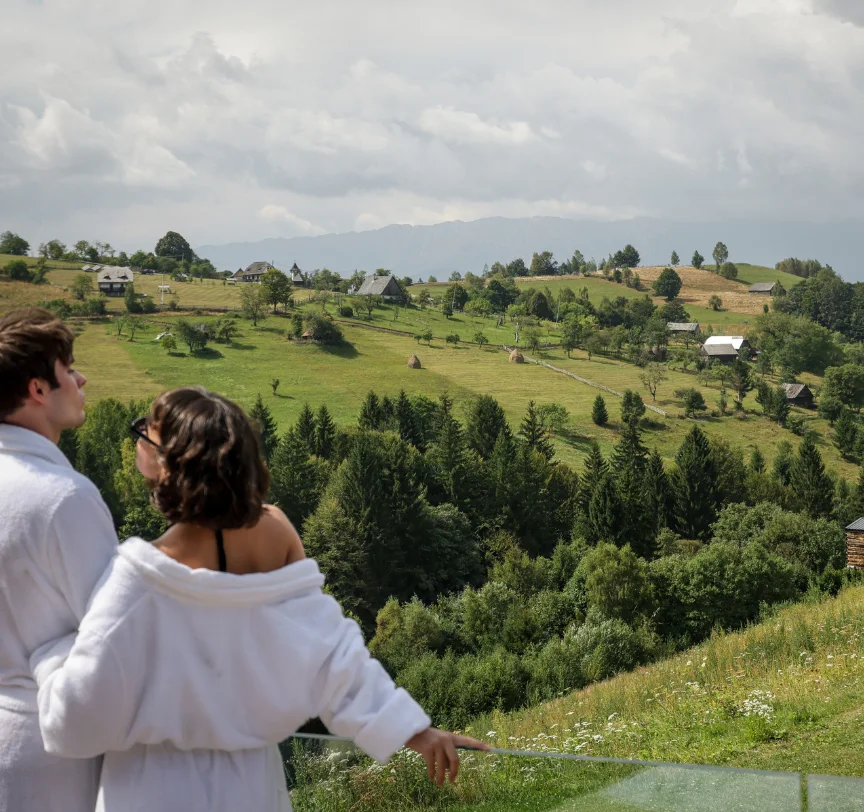 Couple in white robes looking over the green valley from an Eden Hill terrace railing.