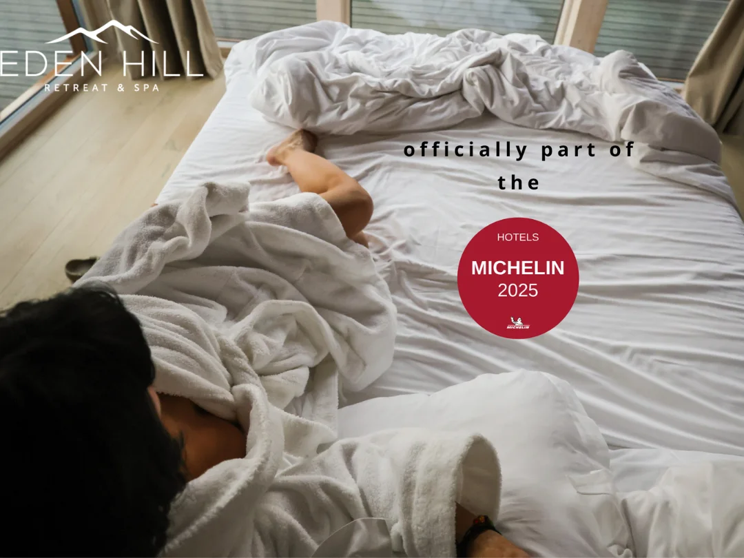 Woman resting in bed beside a window in an Eden Hill composition featuring the Michelin Hotels 2025 badge.